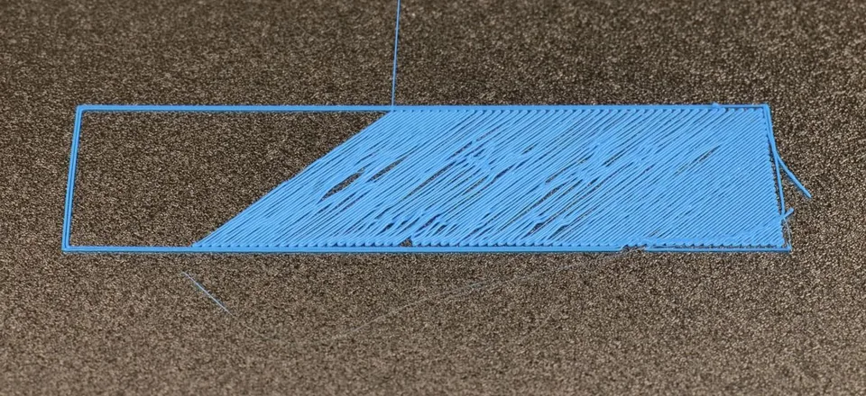Foto di un primo strato fallito sul piatto: il filamento esce a fili staccati e trascinati, e metà del rettangolo resta vuota.